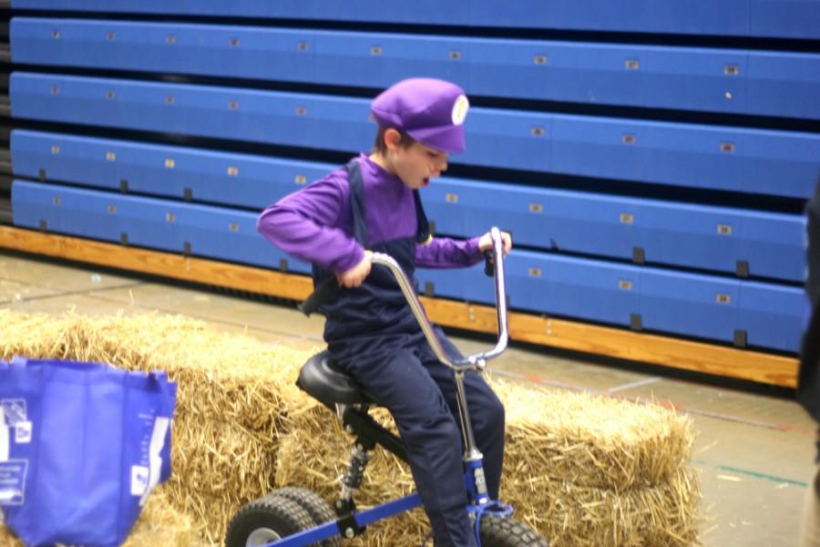 A young child dressed as Wario rides a bike through a hay maze  during Blue Madness in Lantz Arena on Thursday. 