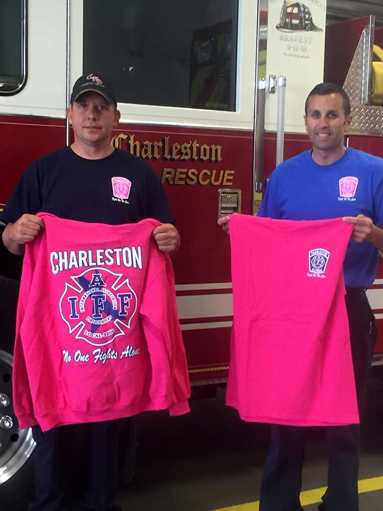 Jason Armstrong, a firefighter and paramedic, and Cire Captain Tim Meister hold up examples of what the shirts look like while standing in front of one of the firetrucks at the Charleston Fire Department.