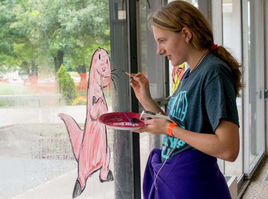 Ashley Colter, a sophomore art major and Andrews Hall council member, paints the windows of Andrews Hall to add some color before students arrive and move into their dorms. Colter said she uses a picture of her subjects as a reference to accurately depict them. “You can do it from memory, but if you want it to look like the actual subject, it helps to have a reference,” said Colter.