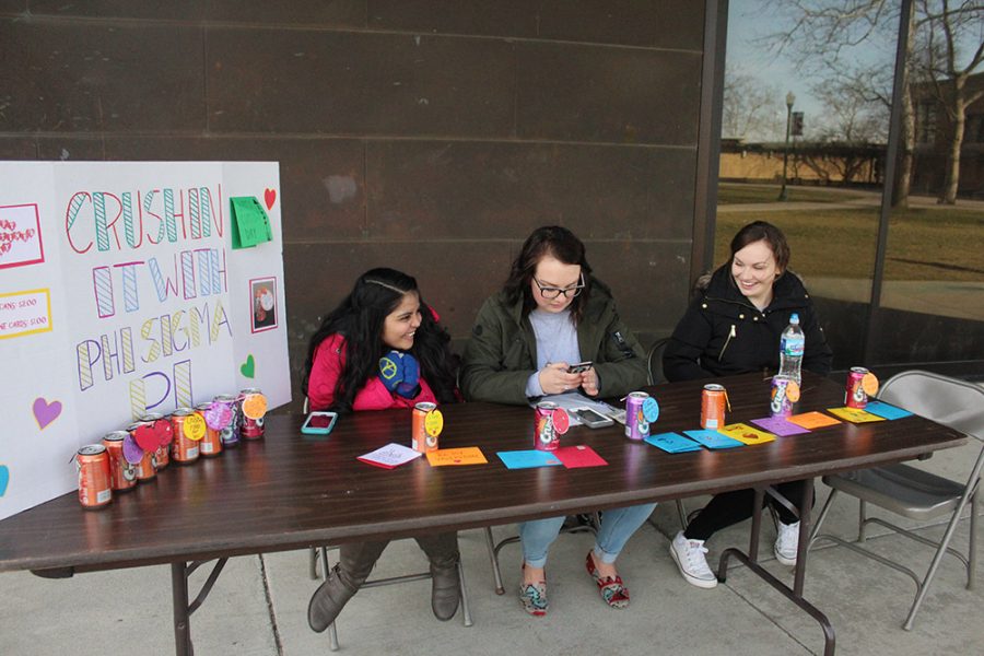 Vidhi Patel, senior kinesiology and sports studies major from Bartlett, IL, Erin Murphy, sophomore neuropsychology major from Troy, IL, and Nicole Estrada, junior psychology major from Bradley, IL sit outside the Doudna Fine Arts Center selling crush cans for Phi Sigma Pi.