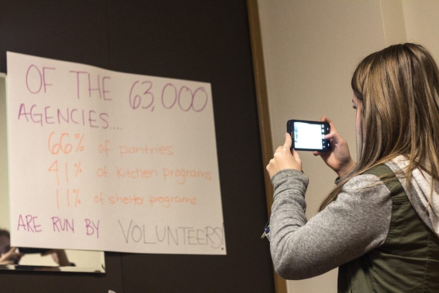 Robyn Mckeown, a senior corporate communications major photographs a sign stating that of the 63,000 agencies, 66 % of pantries, 41 % of kitchen programs, and 11 % of shelter programs are run by volunteers, as part of the tunnel of oppression held in Taylor hall.