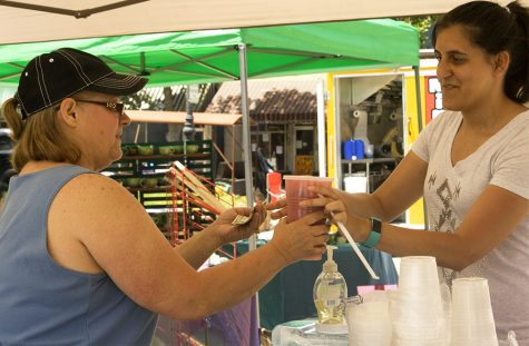 Charleston resident Vicki Brookins hands Alicia Arroyo, a Mattoon resident, a “shake-up” from her stand at Saturday’s Musefest. Brookins started selling the shake-ups, made with ice, sugar, and water, five years ago. Arroyo, in the stand next to her, was selling handmade bath and body products at the arts and crafts festival.
