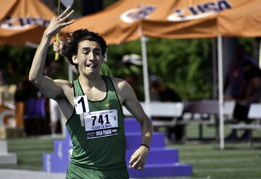 Christopher Collet, a senior from Seneca High School, holds up three fingers, alluding to the triple crown, as he crosses the finish line in first place with a time of 4:24.71 during the final 1600-meter run in Class 1A on May 25. Collet was competing in the Illinois High School Association Boys Track and Field state semifinals and finals, which took place at O’Brien Field May 23 through May 25. He also earned first place in the prelim 1600-meter run with a time of 4:25.16 and first place in the final 3200-meter run with a time of 9:36.99.