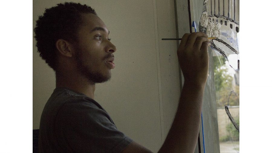 Kelvin White, a sophomore graphic design major and publicity chair of Ford Hall, paints the lobby windows in Ford Hall for Rockfest Sunday afternoon. White said Ford Hall’s theme this year was modes of transportation.