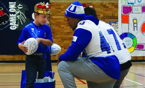 Alex Smith, a junior accounting major, and football player, hands a goodie bag to Eastern’s Little Prince, Mason Koehler, during coronation and pep rally in McAfee Gym on Thursday night. During the pep rally, sororities, fraternities, cheerleaders, and the pink panthers competed in games to win prizes.
