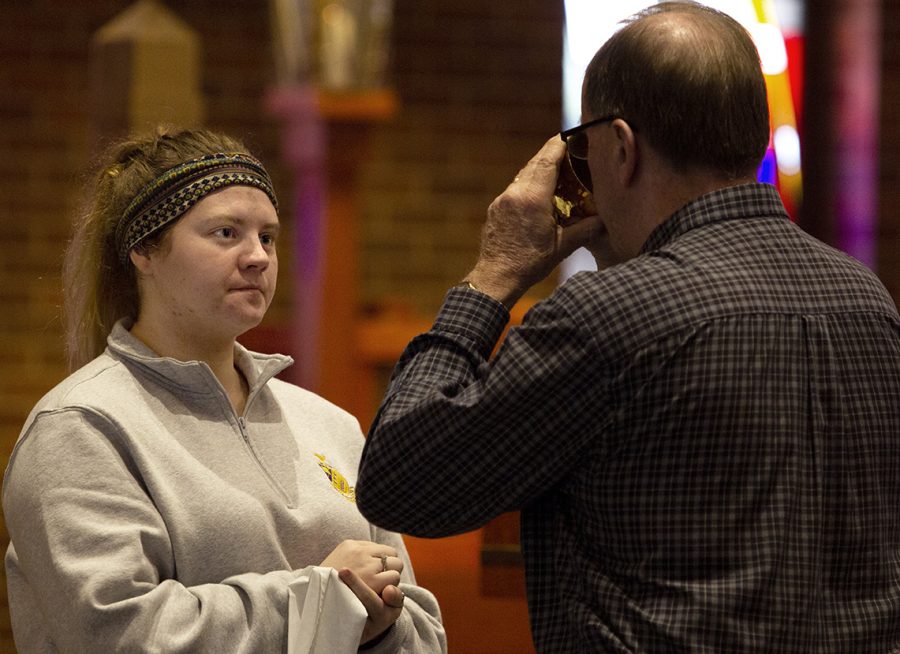Maddie Harvey, a sophomore mathematics major, gives out wine during the Ash Wednesday service in the Newman Center during the noon service. Harvey said she is giving up spending money on herself for lent. “If I spend money, it has to be for other people or for a good cause,” she said.