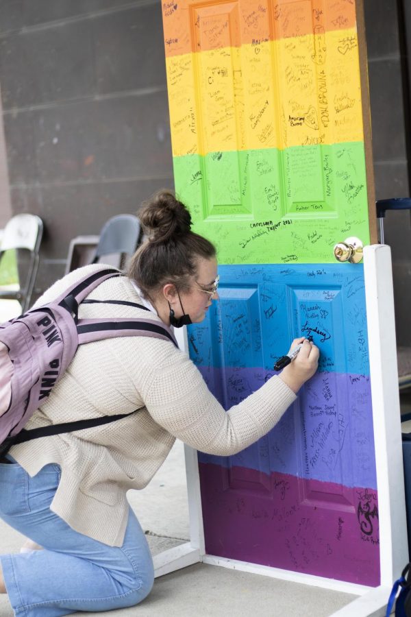 Lindsey Zike, a freshman art education major, signs her name on a rainbow door for National Coming Out Day.