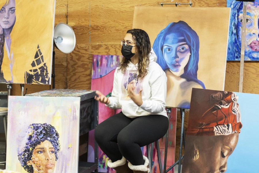 Kendra Moore, a senior art education major, sits in front of 5 art pieces that she has created in Doudna Fine Arts Centers painting studio.