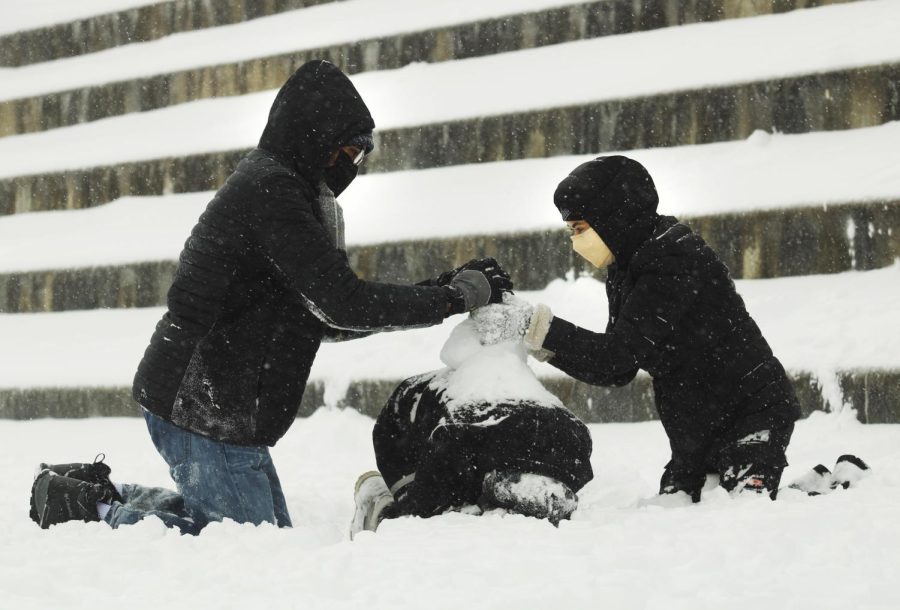 Nathaniel Revish, a junior theatre major, and Waed Al-rifaei, a junior nursing major, build a snowman on the back of Jannah Judeh, a junior biological sciences major, outside on the library quad on Thursday afternoon.