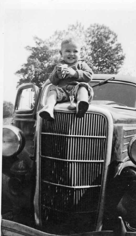 Toddler James Jim Kirby Johnson sits on a car.