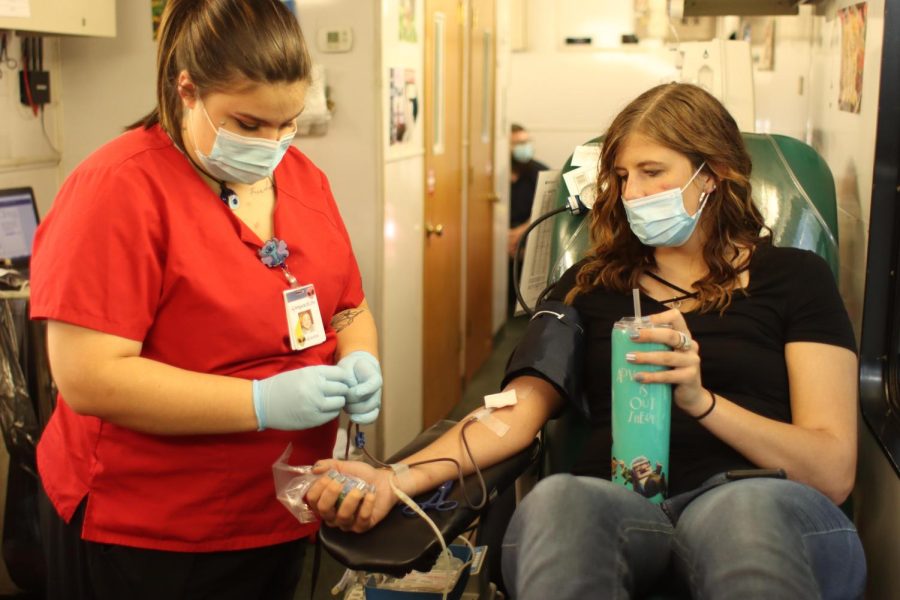 Clarissa Sager (right), a senior business management major, prepares herself before Heaven Bonelli (left) inserts the needle to draw blood Tuesday afternoon in between the Doudna Fine Arts Center and the Union. Bonelli has worked with ImpactLife since January as a phlebotomist for more than two years.