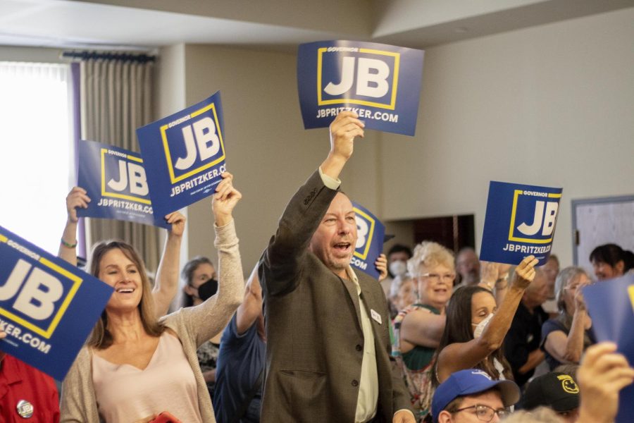 Dave Seiler and other members in the audience cheer and raise up their signs as JB Pritzker, the current governor of Illinois, enters the room of the Charleston Library.
