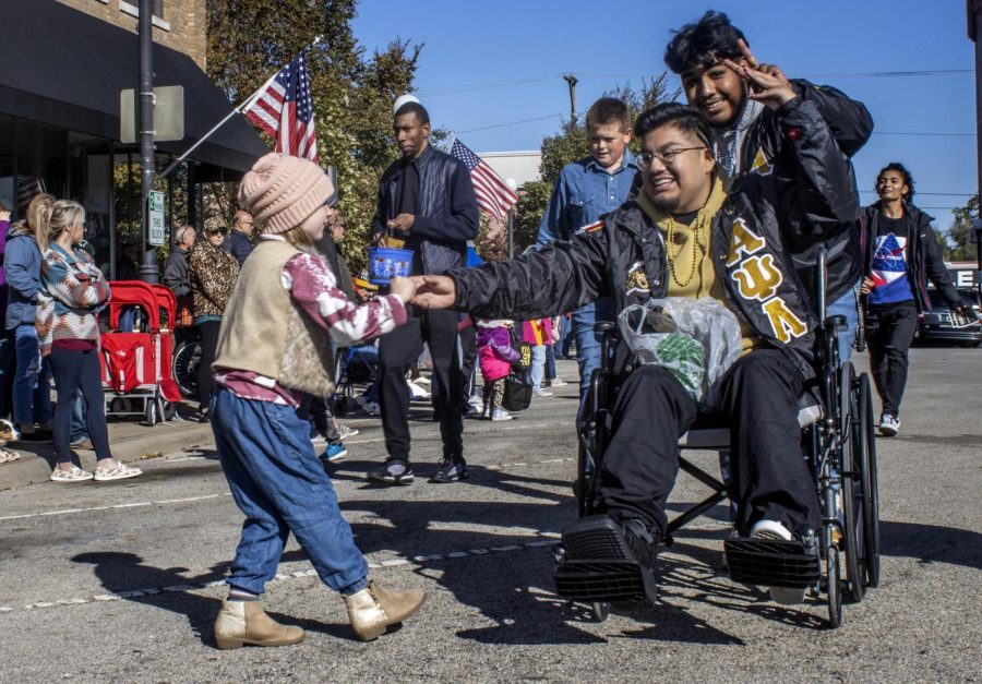 Alpha Psi Lambda President Luis Paniagua, a senior graphic major, hands candy to six-year-old Emma Turner  during the 2022 Homecoming Parade in downtown Charleston at the Square Saturday morning.