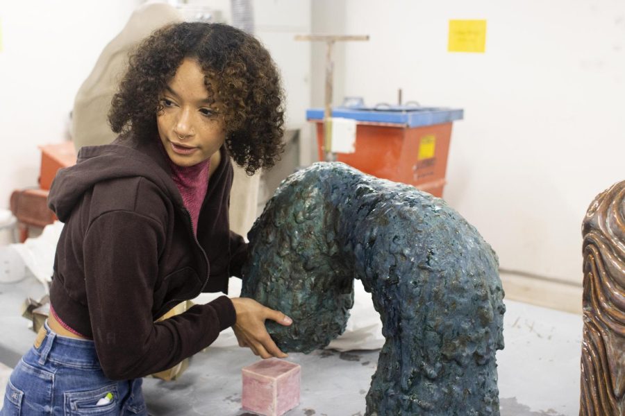 Ashley Spencer, a senior 3D studio major with a focus in ceramics, shows her sculpture named Albert and how the cube piece is connected to it but separate at the same time in Doudna Fine Arts Center Sunday.