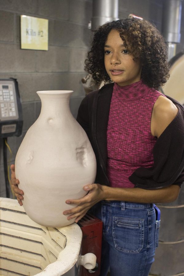 Ashley Spencer, a senior 3D studio major with a focus in ceramics, brings her vessel out of the kiln and explains that the piece is made with three different thrown parts. The bottom part represents feet, the middle part the belly, and then the neck and lips at the top, to overall represent the human body in Doudna Fine Arts Center Sunday.