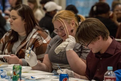 Lindsey Zike (middle), a sophomore art education major, looks up from her painting of Frog and Toad at the Winter Welcome Days Paint and Sip in the University Ballroom Tuesday night. Her friends all said they wanted to buy the painting because it looked so good.