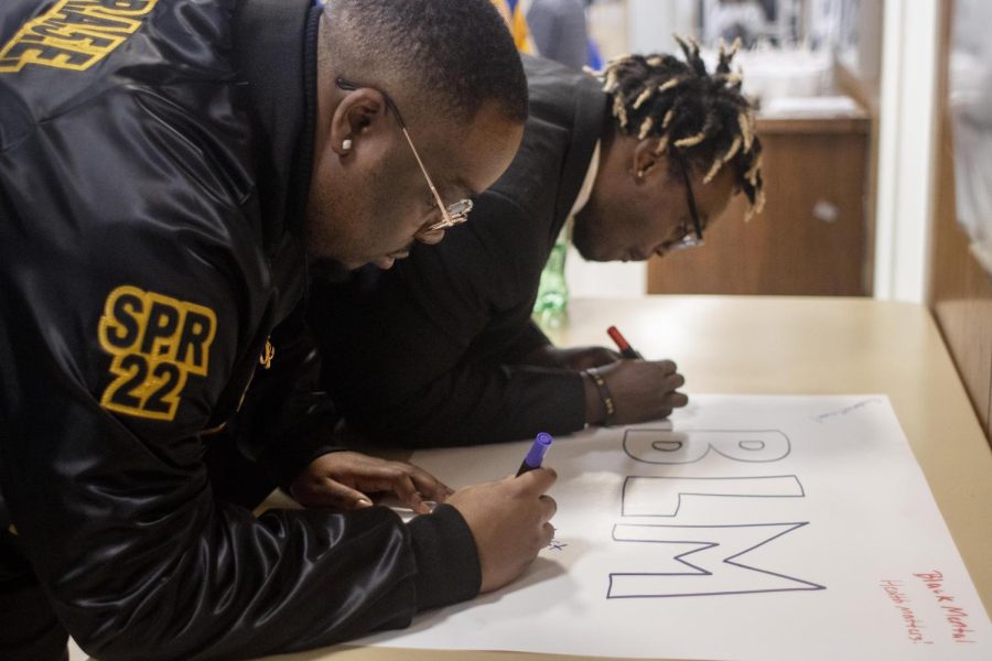 Members of Alpha Phi Alpha Fraternity, Inc., write important messages on posters and encourage others to as well, to hold up while walking in the march for the 36th annual Martin Luther King Jr. program on Monday evening.