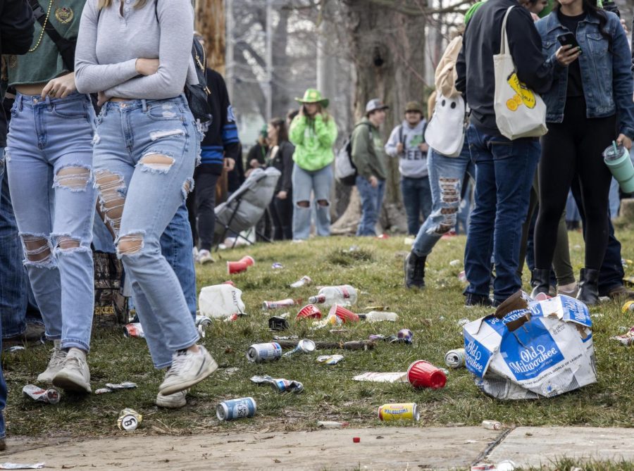 Partygoers walk through and around empty alcohol cans, cups, and 24-packs at the third Unofficial party house Saturday afternoon. The party was canceled after there was damage to the property and an individual left in an ambulance. 