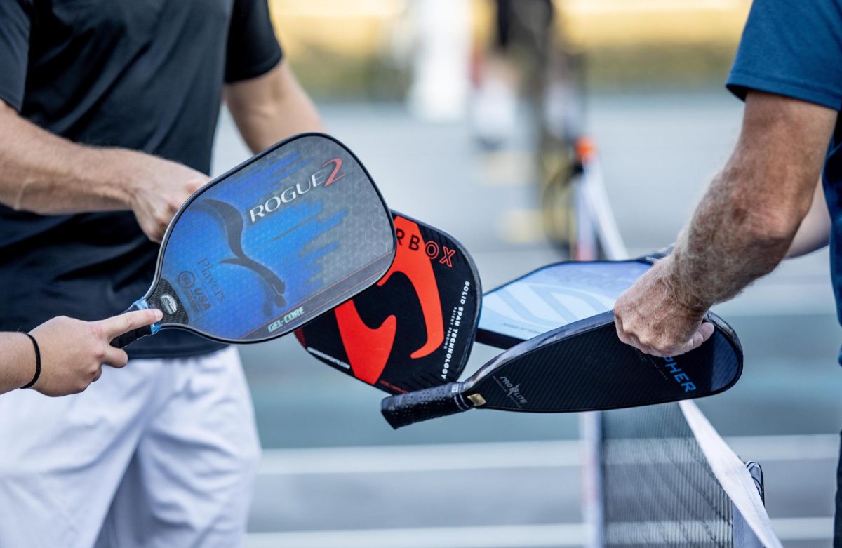 A team of pickleball players touch their paddles after a game at the outside Lantz Arena tennis courts.