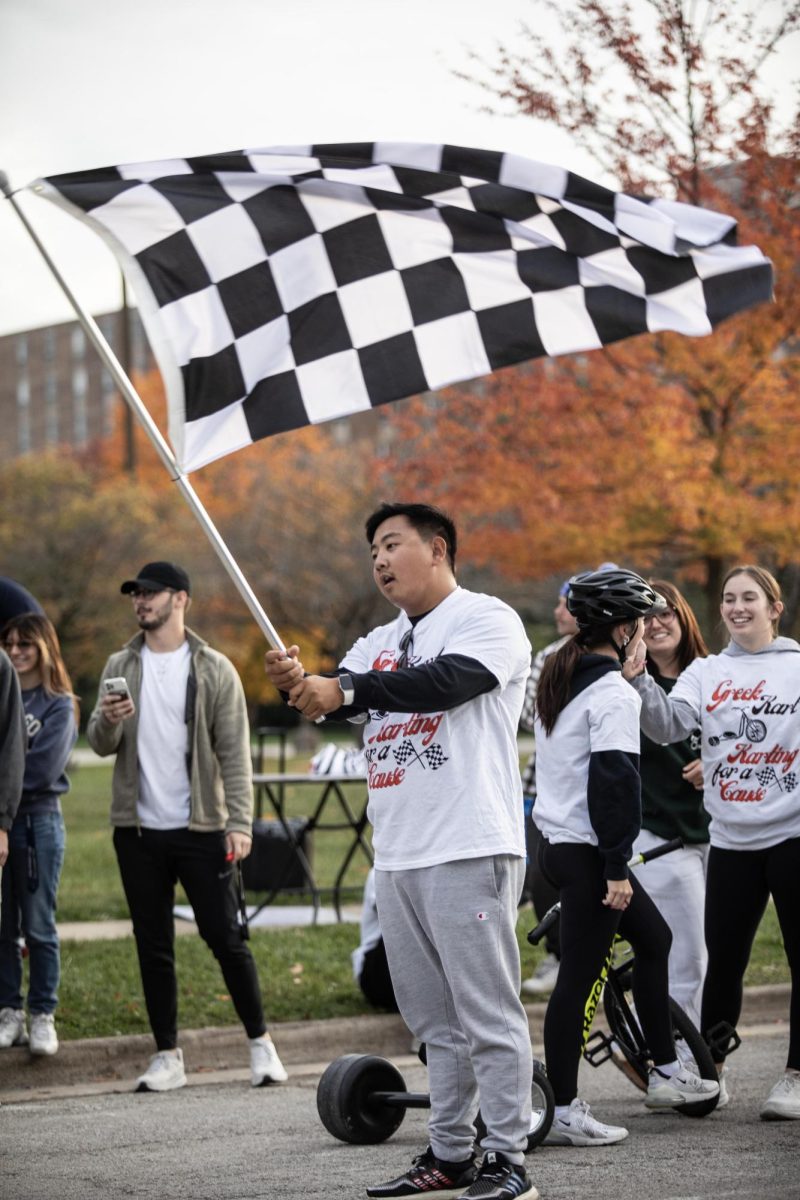 Michael Barth, a senior physical education major, waves the race flag as the last team passes the finish line at the Greek Kart Race for Roman event.