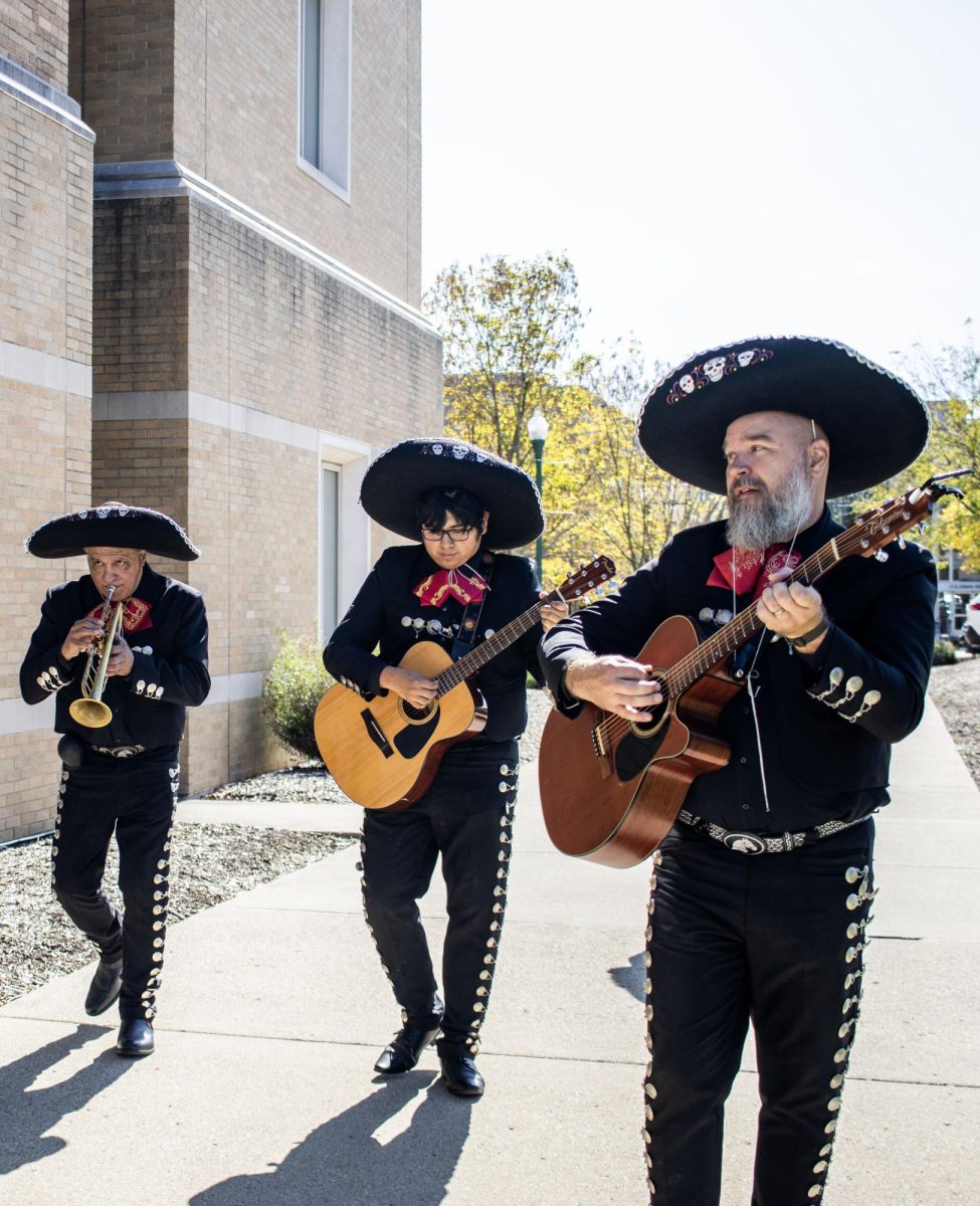 From left, Luis Trevino, the band leader of Los Amigos, plays the trumpet, while Elvis Vasquez and Mike McAllister play their guitars while walking past Booth Library.
