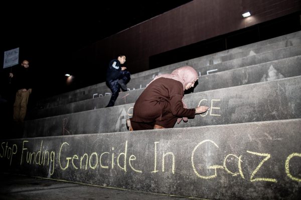 Tahani Bilkhair writes Stop the genocide on the Mellin steps during a vigil for Gazas children.