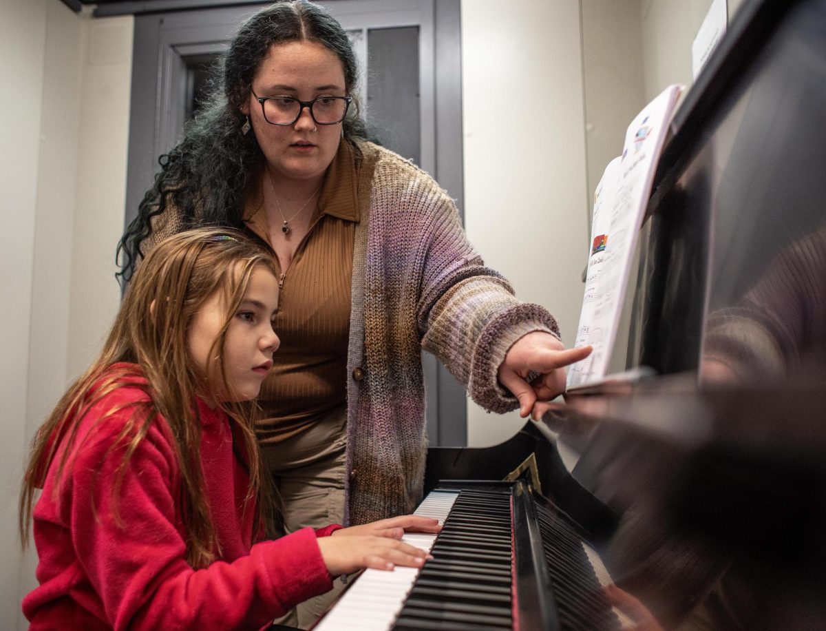 Jemma Allen, a junior vocal performance and music education major, instructs Madison More, 8, a student at Carl Sandburg Elementary School, on which notes to play on the piano in a practice room in the basement of the Doudna Fine Arts Center Thursday. 