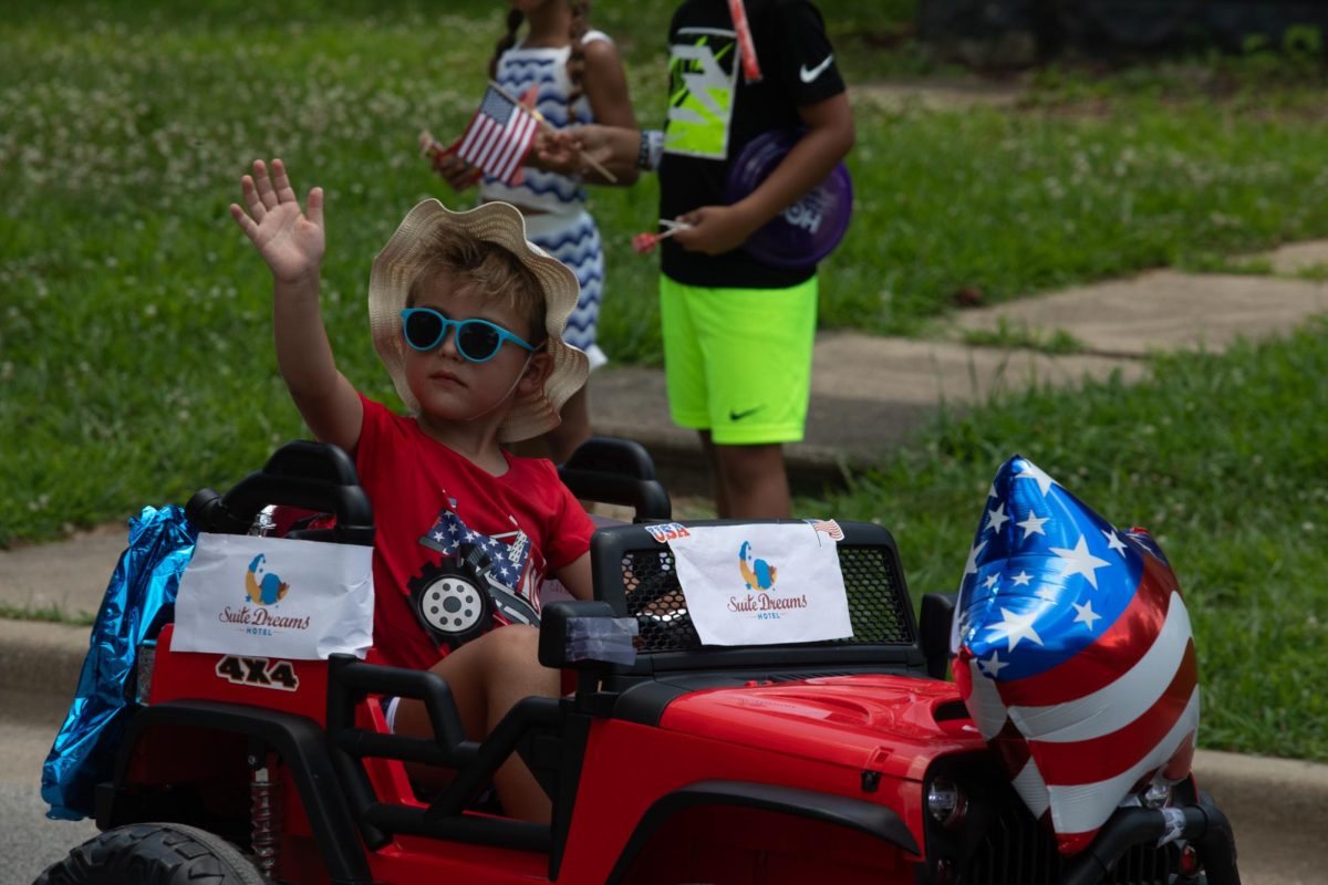 A kid in the Charleston 4th of July Parade waves towards the crowd while driving a toy car on Polk Ave in Charleston, IL on July 4.