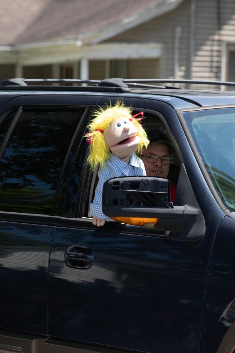 A puppeteer with a blonde puppet peeking out of a vehicle window during the Charleston Fourth of July Parade on Polk Avenue in Charleston, Ill., on Thursday, July 4, 2025.