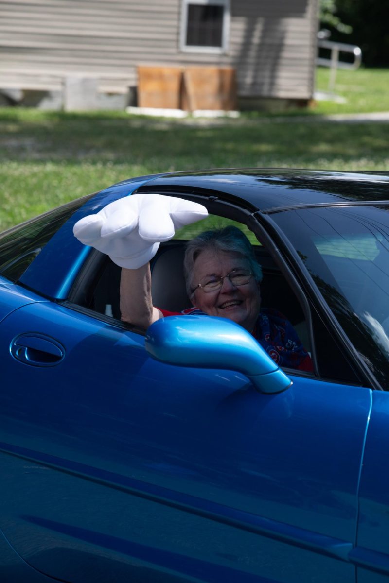 A woman in a blue Chevrolet Corvette apart of the line of Corvette cars waves to the crowd with a big white hand during the Charleston Fourth of July Parade on Polk Avenue in Charleston, Ill., on Thursday, July 4, 2025.
