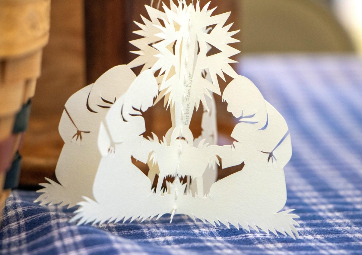 A papercut nativity scene made by Barbara Dyar sits on a blue and white tablecloth at Harvest Frolic at the Lincoln Log Cabin on Sept. 28, 2025, in Lerna, ILL. This piece was made by folding paper and cutting it with surgical scissors to make two symmetrical halves.