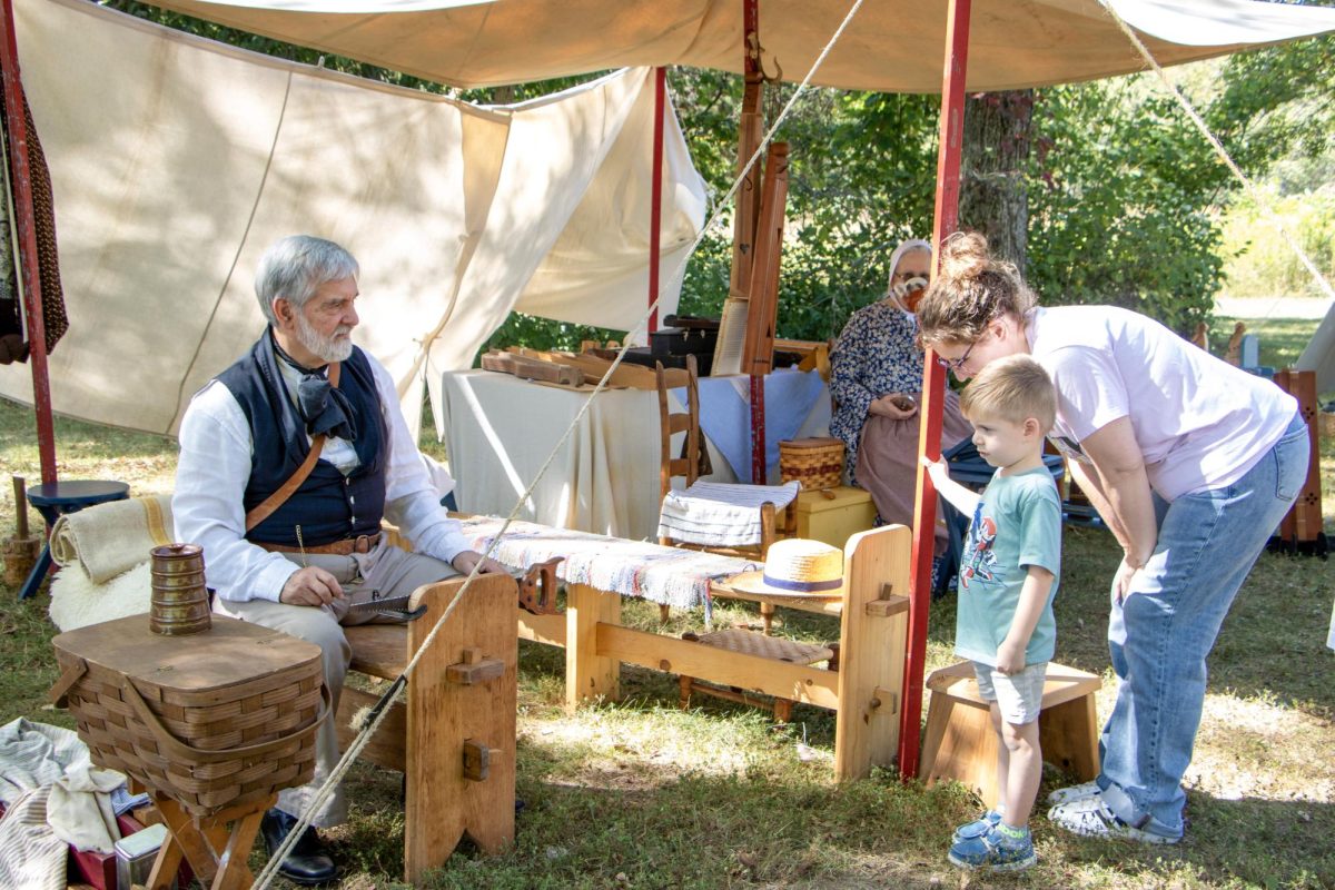 Woodworker Steve Vann (Left) and Jen Easten (Right) encourage 4-year-old Johnathan Easten (Middle) to help sharpen a saw at Harvest Frolic on Sept. 28.
