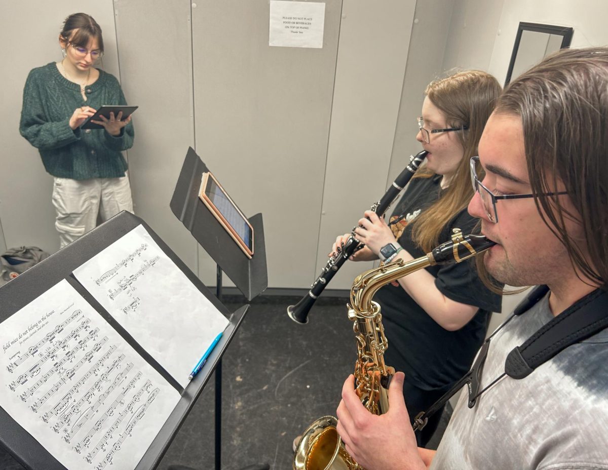 Senior music composition performance major and “Field Mice Do Not Belong in the House” composer Alene Maxstadt (left) follows alongside junior music education major Kate Aldridge (middle) and junior music education major Kyle Rennier (right) as they use Maxstadt sheet music during rehearsal in a practice room in the Doudna Fine Arts Center on Sunday.