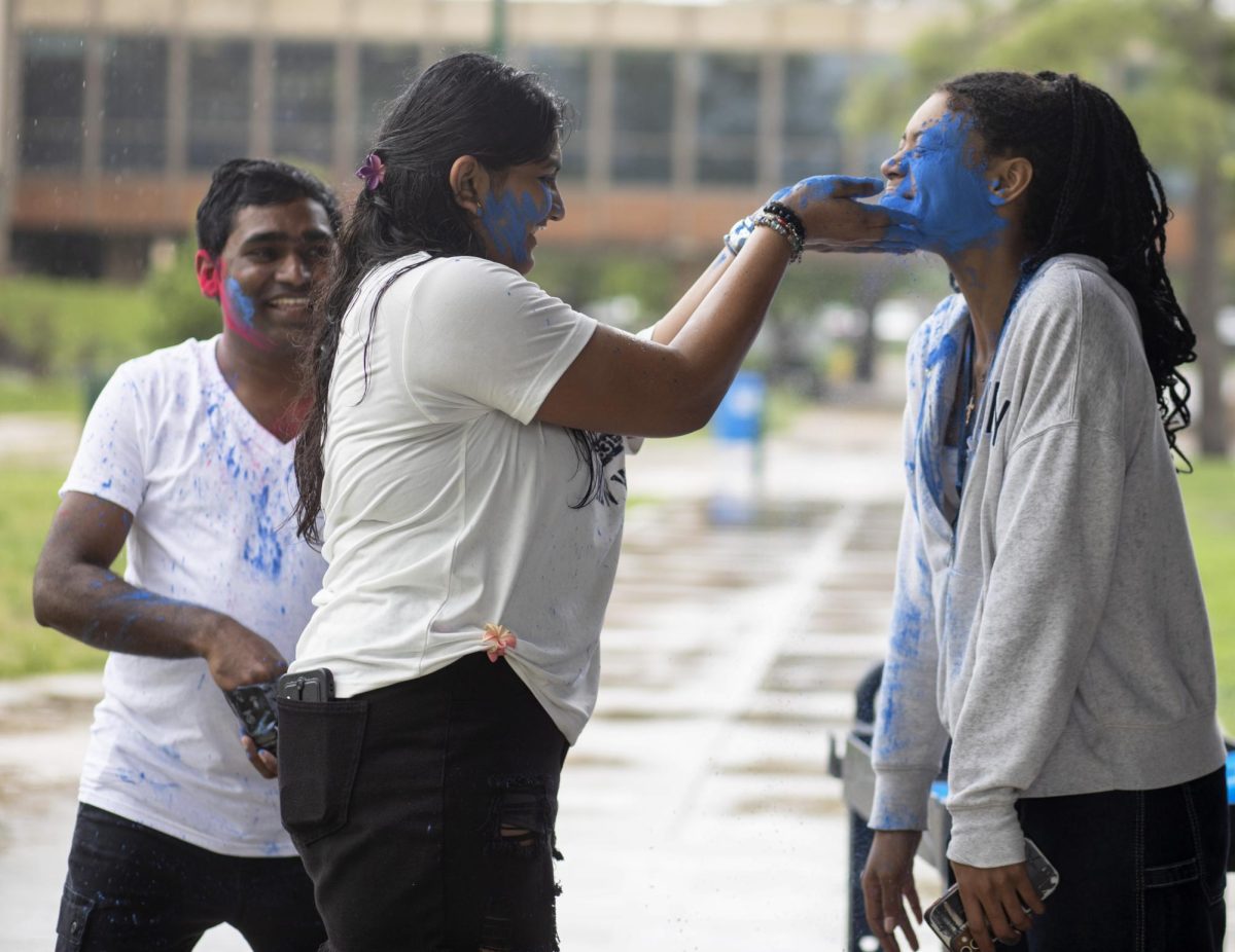 Computer and informational technology major Vani Patel (middle) puts blue pigment onto psychology major Ajah Crawford (right) at Holi Color Fest on Friday on the Library Quad. Patel is the president of Indian Student Association on EIU's campus, which hosted the Holi Color Fest alongside Association of International Students. 