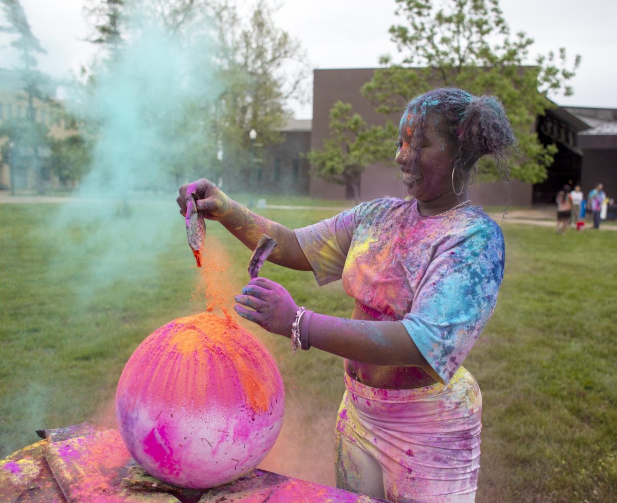 Jamaya Fuller pours pigment onto a ball at Holi Color Fest on the Library Quad. She would later kick the ball into the air, making the pigment fly around.