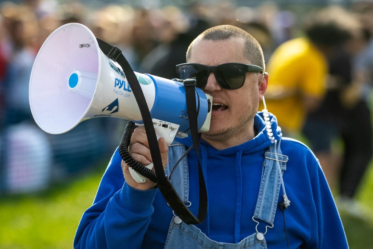 Nathan Wehr speaks into a megaphone to inform the participants at the Tugs event during the Greek Week Tug of War activities across the campus pond on Wednesday afternoon.