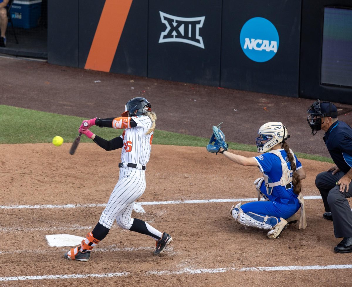 Oklahoma State University softball junior infielder Rosie Davis (left) goes to hit a ball as junior catcher Sophia Olman (right) waits for the ball during EIU’s 16-0 loss to Oklahoma State University in the second game of the NCAA Stillwater Regional on Friday.